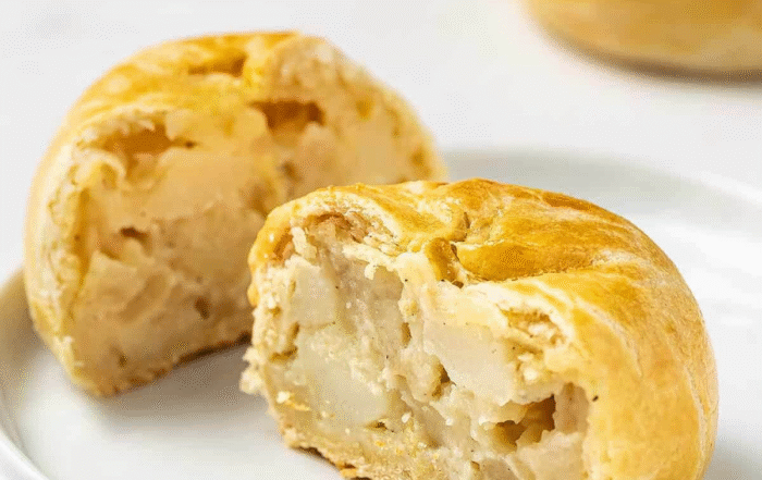Cut potato-stuffed pastry showing creamy filling, on a white plate with whole pastries in the background.