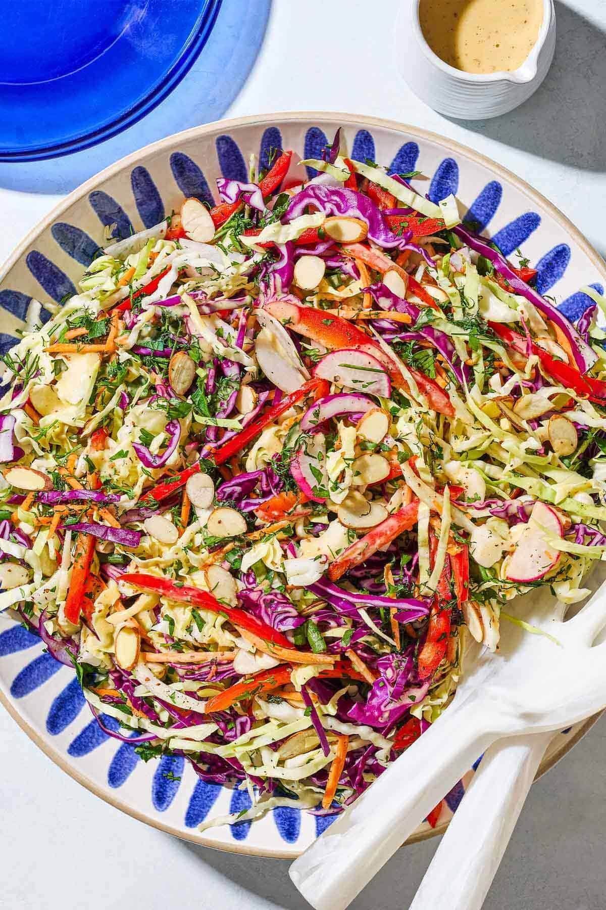Crunchy green and purple cabbage coleslaw with carrots, tossed in lemon dressing, in a glass bowl with a spoon, lemon wedges, and pepper nearby.
