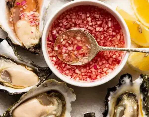 Fresh Oysters with Classic Mignonette Sauce Fresh oysters on ice with a bowl of mignonette sauce (shallots in red vinegar) and lemon wedges, with a spoon in the sauce.