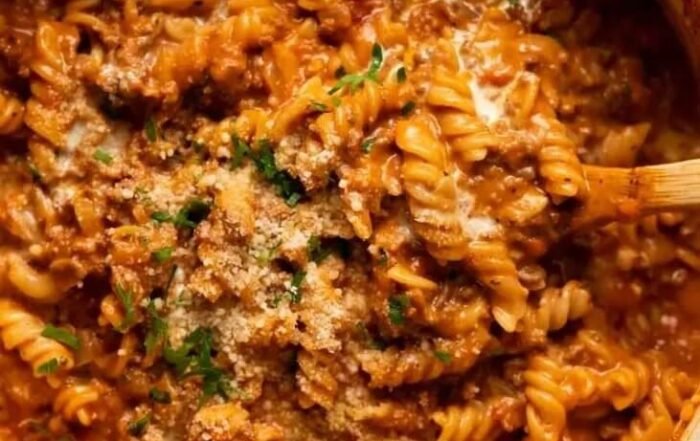 Two bowls of teriyaki chicken rice with broccoli, carrots, red peppers, scallions, and sesame seeds, one bowl held by a hand, with garnish dishes and gold forks nearby on marble.